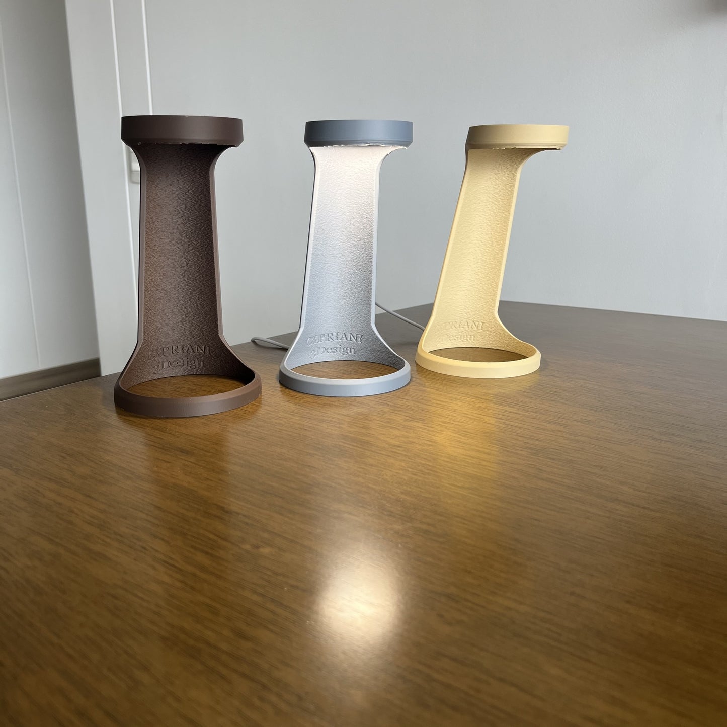 Grupal: variantes Chocolate, Desert Tan y Ash Gray juntas apagadas sobre mesa de madera, fondo pared blanca