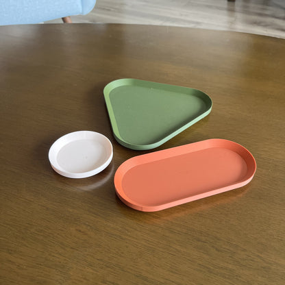 Bandejas grupal separadas vacias (oval terracota, triangular verde oliva mate, plato redondo beige) sobre mesa de madera, angulo alternativo desde otro punto