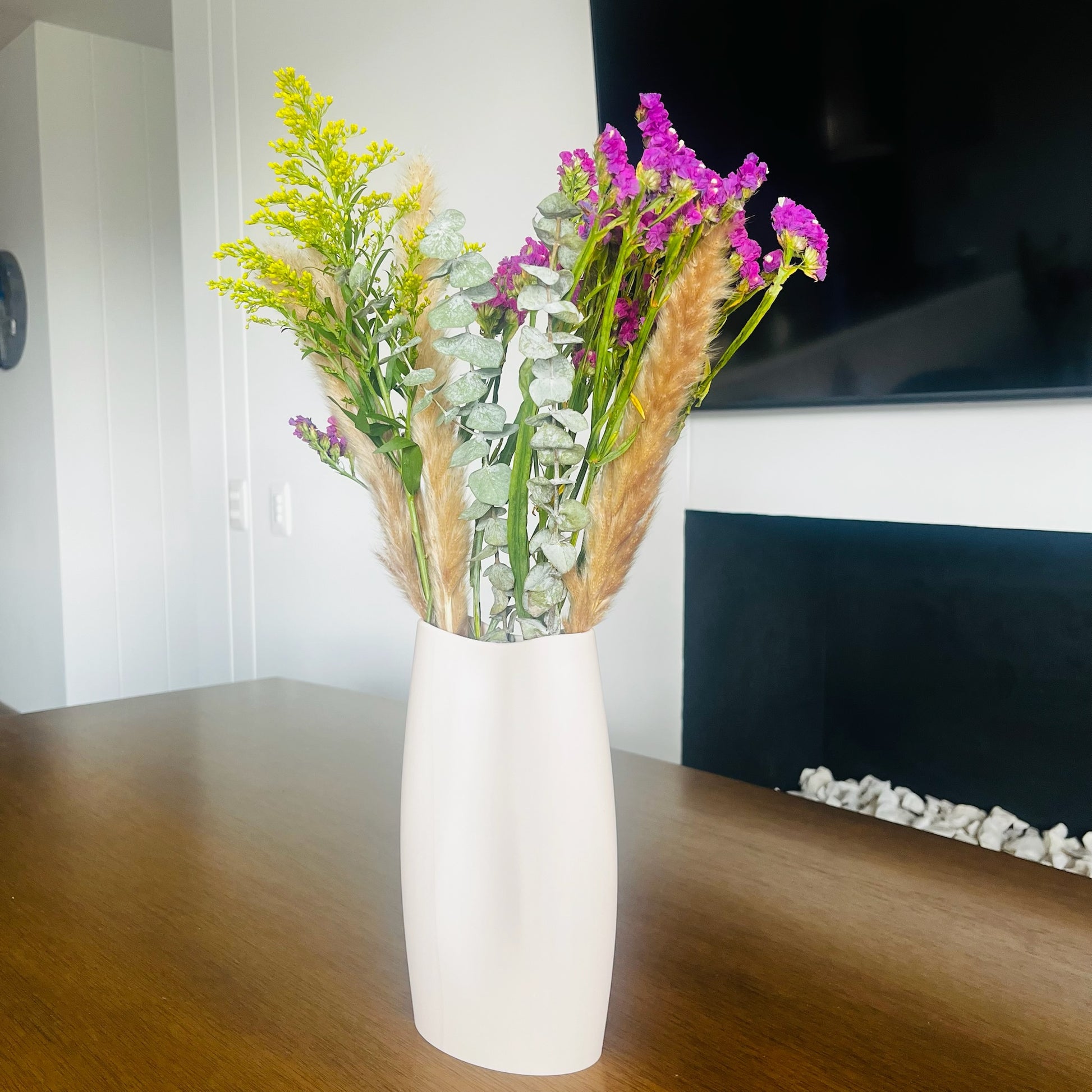 Jarron beige con flores secas y frescas, sala con chimenea y TV, luz natural