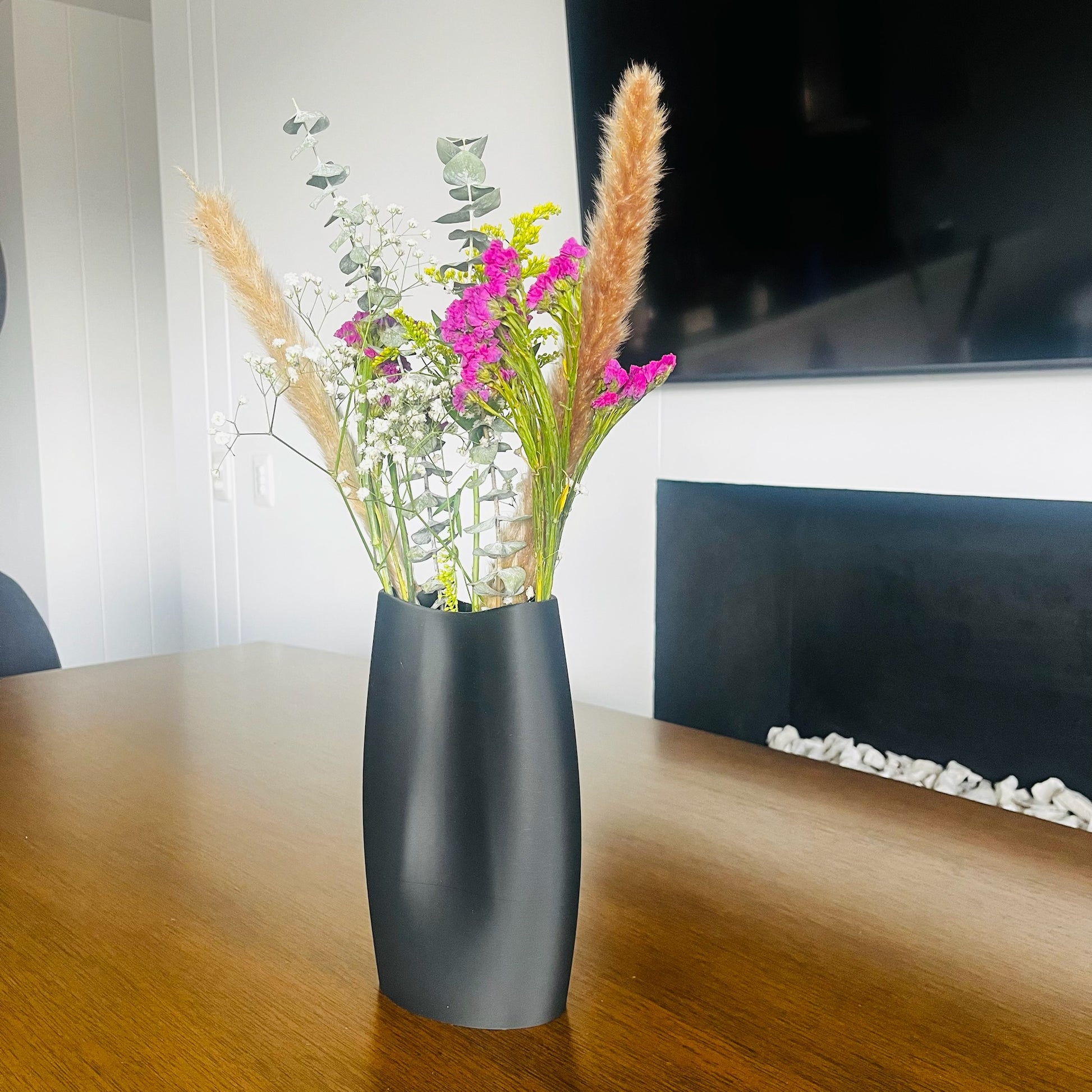Jarron charcoal con flores secas y frescas, sala con chimenea y TV, luz natural