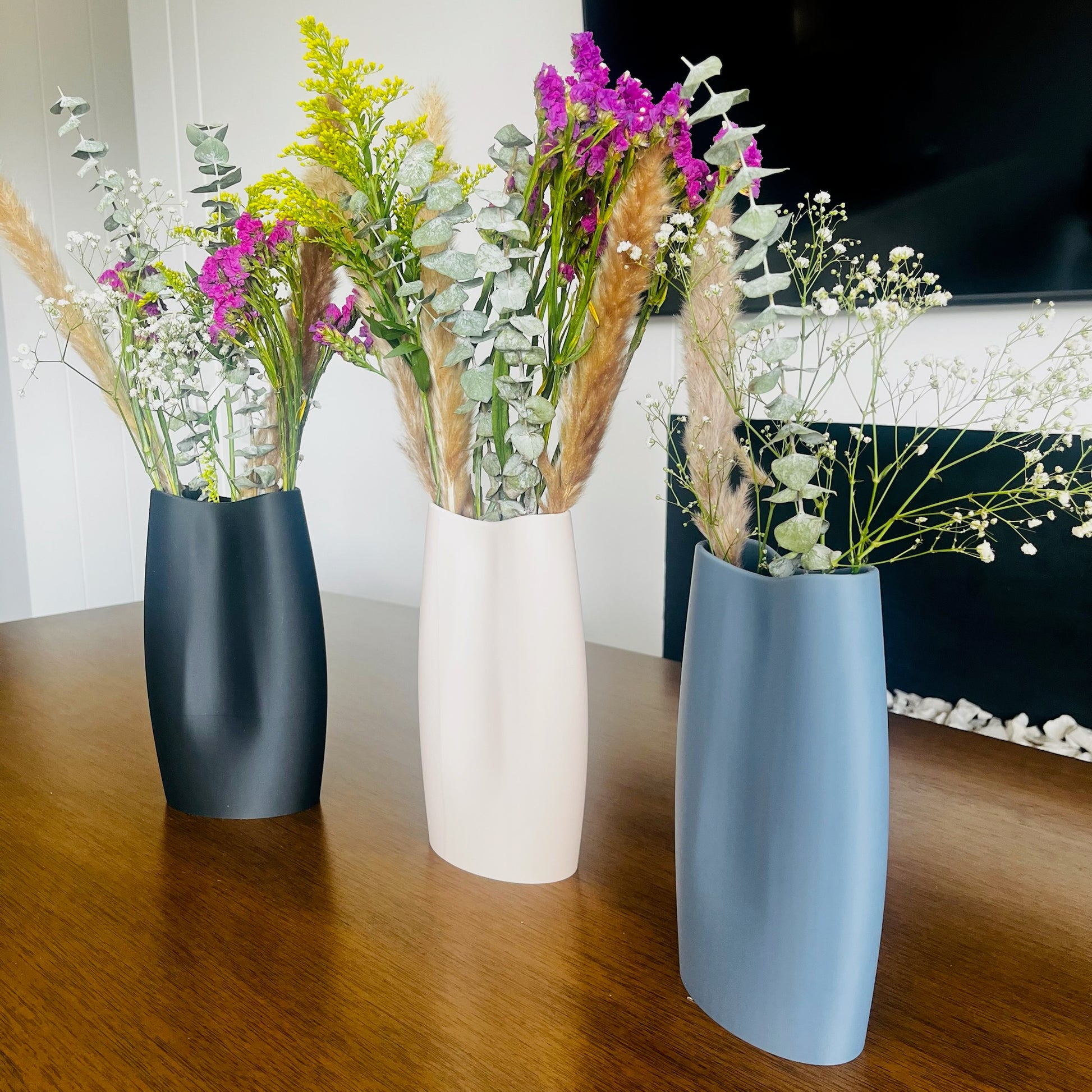 Los 3 jarrones (beige, charcoal, blue grey) con flores, vista grupal en uso con las 3 variantes