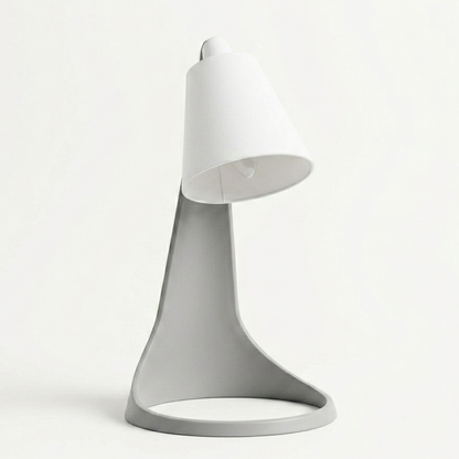 Lampara Curva Ash Gray + Blanco encendida con bombillo visible, en escritorio con monitor y ventana de fondo