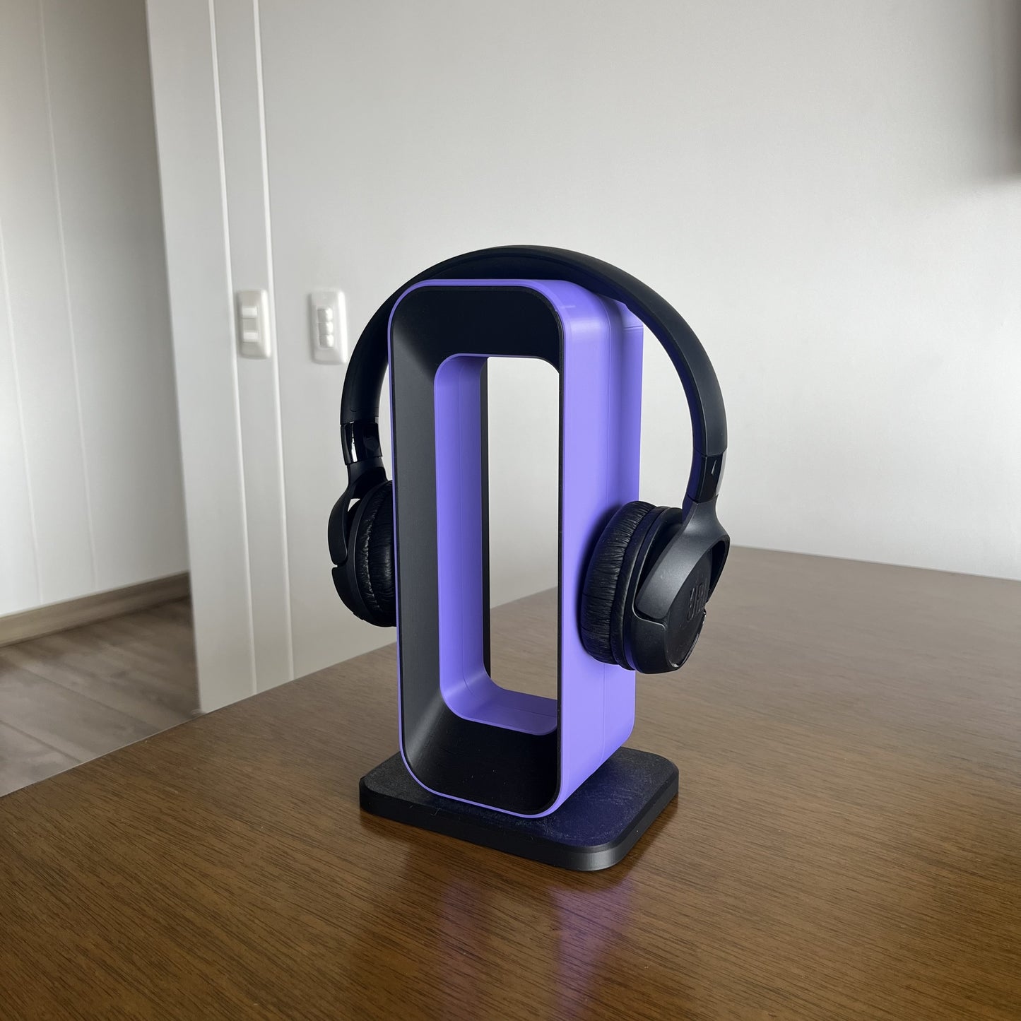 Soporte Charcoal + Purple con audifonos JBL negros puestos, mesa de madera, fondo blanco limpio